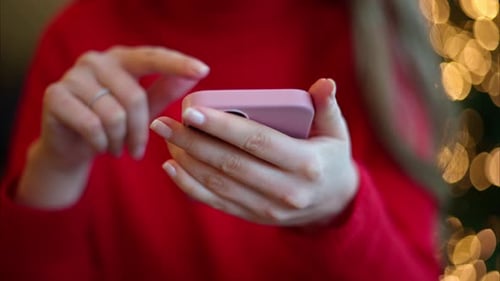 Woman in red sweater using smartphone. Green tree with lights on background