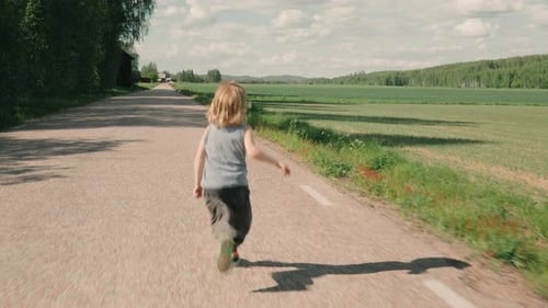 Criança corre ao longo de uma estrada rural de asfalto ao lado de campos agrícolas