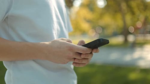 Adolescente sostiene un teléfono celular en la mano mientras está de pie en un parque