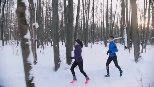 Young Man and Woman Running in Winter Forest at Early