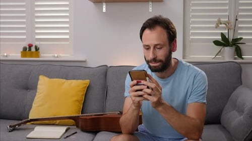 A STATIC SHOT in a minimalistic lounge of an average man texting and smiling on his smart phone.