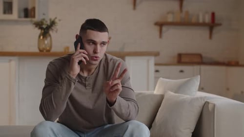 A Darkhaired Man Sitting in a Home Office is Discussing Something on the Phone and Gesturing with
