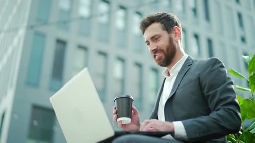 Smiling Man Works on Laptop With Coffee Outdoors