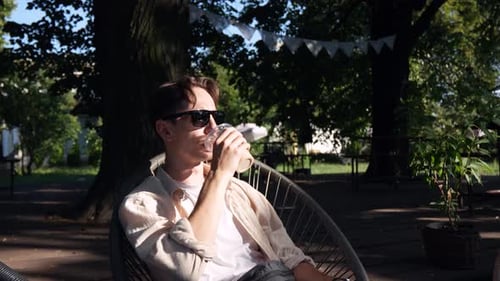 A young guy with glasses drinking a cold drink on a summer terrace
