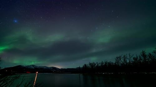 Vibrant northern lights dancing in starry night sky, time lapse view over river