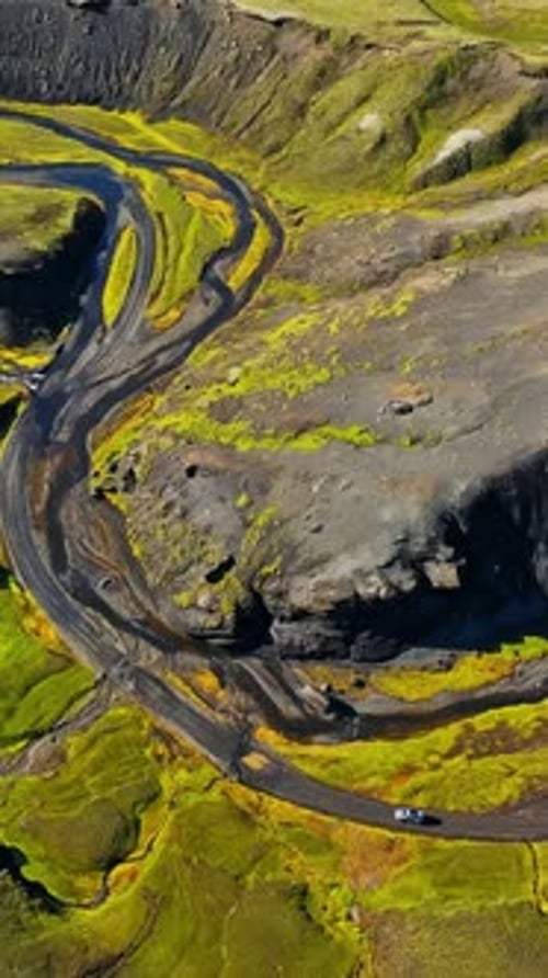 Vertical drone view of a 4x4 crossing braided streams on a winding black volcanic road in Icelandic
