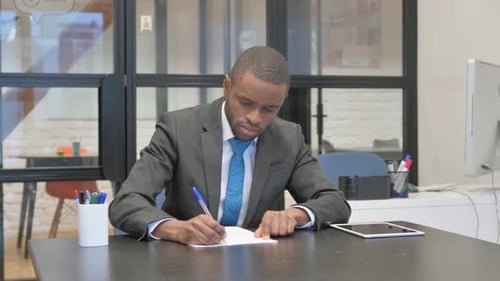 Man Writing at Desk in Modern Office Environment