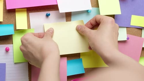 Die Hände einer Frau kleben eine Notiz in Papierform auf eine Erinnerungstafel. Konzept der Geschäftsidee.
