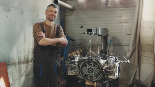 Male caucasian car mechanic at a service station smiling happy after engine repair with broken car