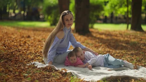 Young Mother with Children Resting on a Blanket in an Autumn Park Concept of Happy Family Moments