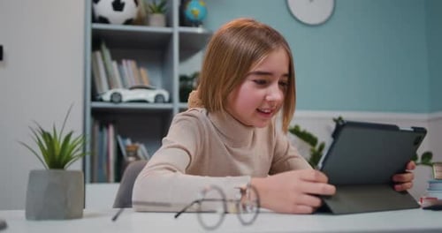 Una niña linda y feliz usa una tableta mientras está sentada en el escritorio de la sala de estar.
