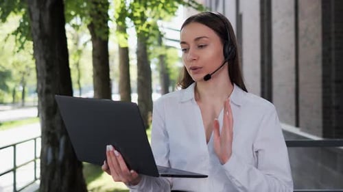 Woman With Laptop Talking on Headset Outdoors