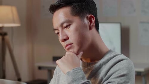 Close-up de um homem asiático pensando enquanto trabalhava com uma mão ciborgue em um laptop em casa