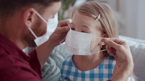 Adult Putting Protective Mask on Young Child