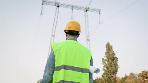 Energy Auditor Approaching Electricity Pylon on Construction Site