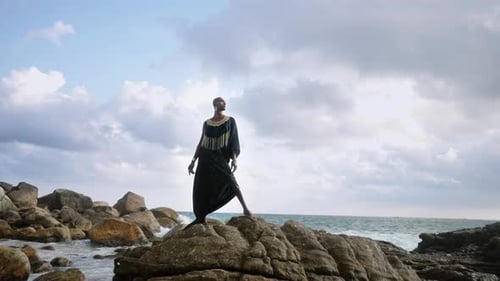 Gay Bipoc Man in Luxury Dress Boutique Brass Jewelry Makeup Poses Gracefully Tropical Rocky Hill Top