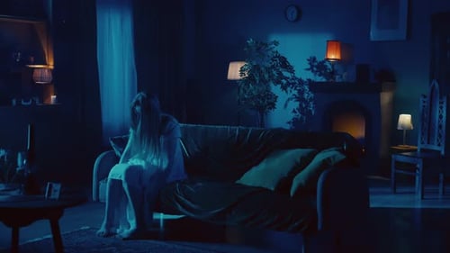 Sad Woman Sits Alone in the Dark on Sofa