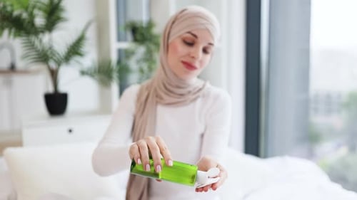 Young Muslim Woman Cleansing Skin with Green Bottle Skincare Product
