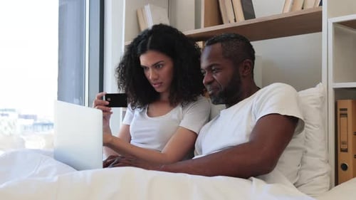 Couple Relaxing in Bed with Laptop and Phone