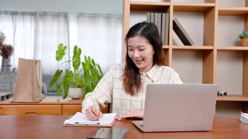 Beautiful Asian office worker, sitting working on laptop computer placed on table in front, with car