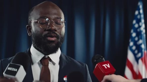 Man Speaks at Press Conference with Microphones