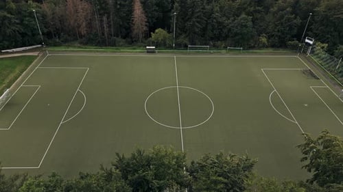 Aerial Flight besides an empty, green football field in the middle of the forest, Drone Footage