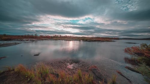 Stormy clouds move fast in the sunset skies as darkness falls upon the calm river and grass-covered