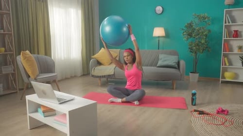 Una Mujer Sentada Con Las Piernas Cruzadas Sobre Una Colchoneta Deportiva Ve Una Lección En Un Vídeo En Un Ordenador Portátil Mujer Afroamericana