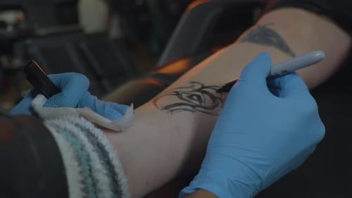 a tattoo artist sketches the pattern for a rose tattoo onto the clients leg in preparation for ink