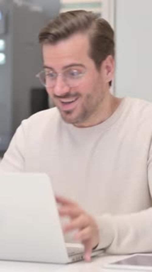 Excited Young Man Celebrating Success on Laptop in Office
