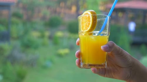 Hand Holding Orange Juice with Orange Slice Garnish