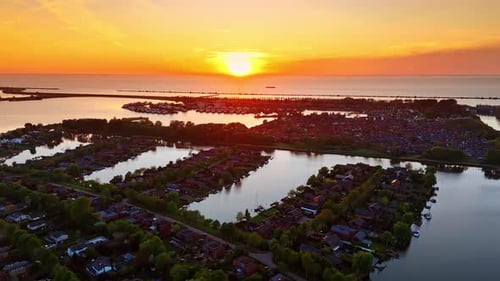 Flight over the picturesque village located on the water. Sun sets over the waterscape at backdrop.