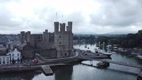 Ancient Caernarfon castle Welsh harbour town aerial view medieval waterfront landmark reverse reveal