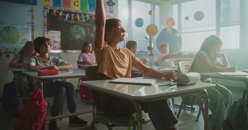 Primary School Children Sitting at the Desks Raising Hands to Give Correct Answer