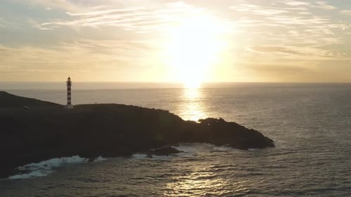 Panorama-Drohnenaufnahme eines Leuchtturms zur goldenen Stunde mit Meer und Sonne