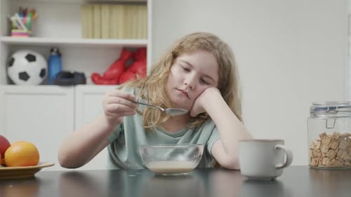 Tired Girl Slouching at Table while Eating Cereal