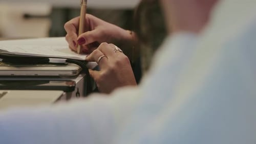Close up of hands writing in notebook with pen on desk