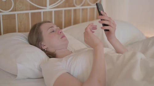 Young Woman Lying in Bed Using Cell Phone