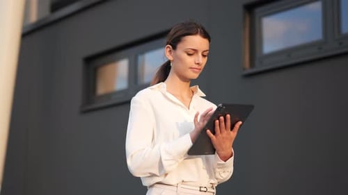 Businesswoman walking walking past modern building with a tablet in her hand