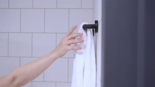 Hand slowly pulling a clean white bath towel off a hanger in the bathroom at home or in a motel. Tra