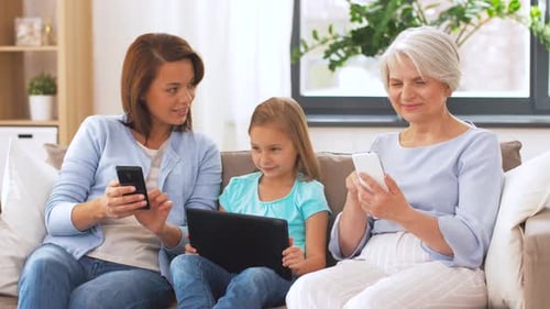 Three generations of women using devices on sofa
