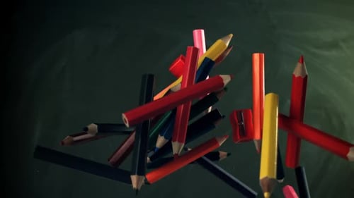 Multicolored Pencils Flying Against the Background of a Blackboard Filmed on a Highspeed Camera at