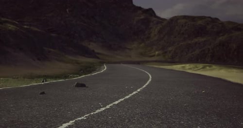 Winding Road Through Mountains Under Cloudy Sky at Dusk