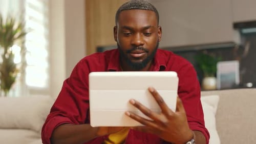 Happy African American Young Man Using Digital Tablet Computer at Home Sitting on Sofa Handsome