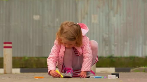 beautiful little blond girl at the park draws with colored chalks