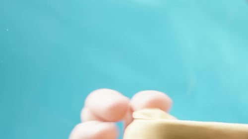 Mit einem gelben Mikrofasertuch wischt eine Hand das Glas ab. Auf blauem Hintergrund, Ansicht von der Rückseite
