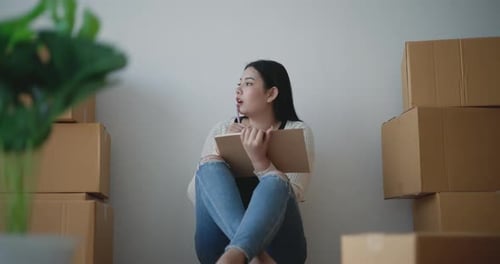 Woman Sits with Moving Boxes, Taking Inventory