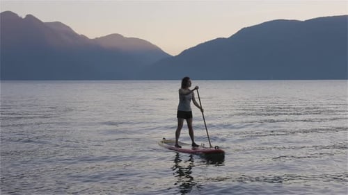 Adventurous Woman Paddling on a Paddle Board in a Peaceful Lake