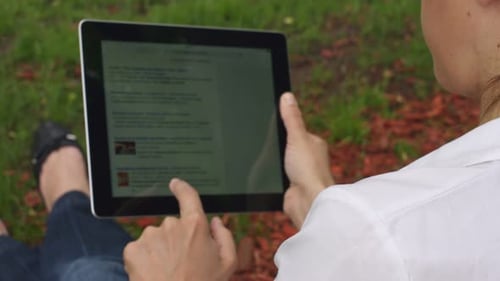 caucasian woman sitting in the grass park with tablet