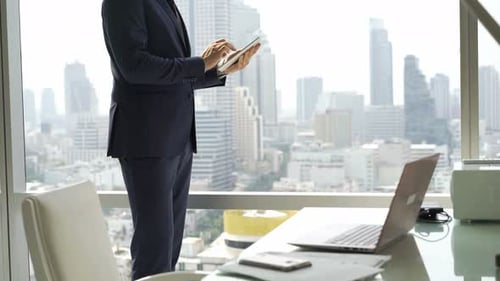 Smiling businessman using tablet computer stands by window in modern office
